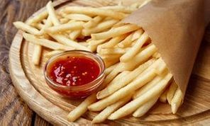 French fries wrapped in brown craft paper, closeup. Fast food take away on rustic wood. Fried potato chips with tomato sauce.
